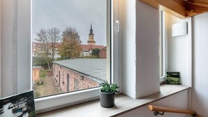 Huoneessa on suuri ikkuna, ikkunalaudalla on ruukkukasvi, puinen penkki ja valokuvakehys.