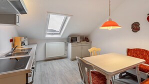 A compact kitchen with a microwave, sink, and stove, a dining area with a table and chairs, a skylight, and a hanging light fixture.