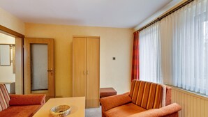 A room with a sofa, a table, a wooden wardrobe, and a window with curtains.