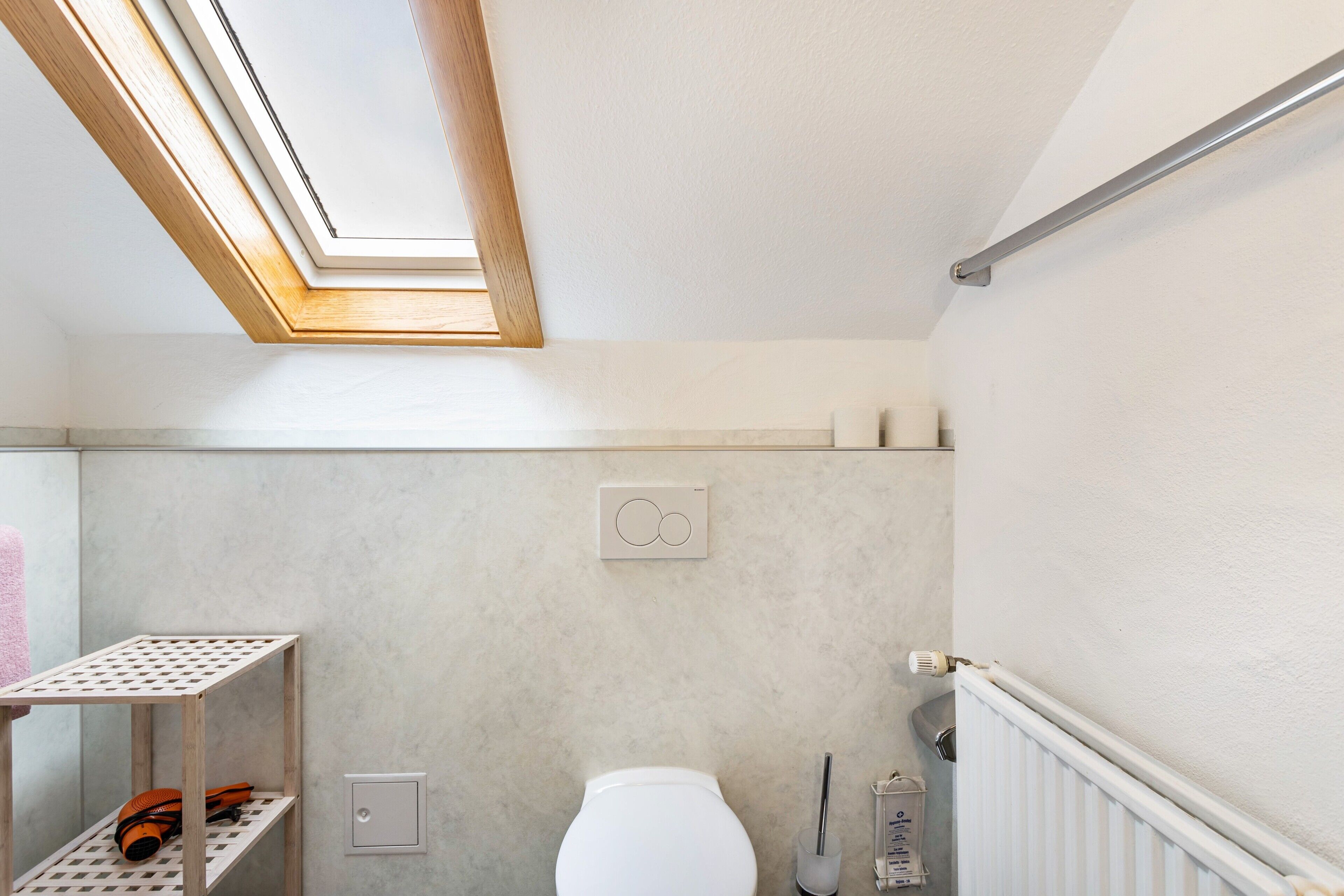 Un bagno con una finestra sul tetto, un water, uno scaffale con asciugamani e un termosifone.
