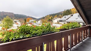 Ein Balkon mit Holzgeländern, der auf einen Wohnbereich mit Häusern und einen bewaldeten Hügel blickt.