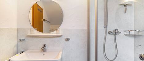 A bathroom with a white sink, a round mirror, a shower with a handheld showerhead, and a glass-enclosed shower stall.