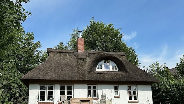 Una casa blanca con techo de paja, una chimenea y un banco en el exterior.
