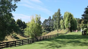 A grassy field with a wooden fence and trees in the background. - The Orchard & Oak Apartment - Pool, Peaceful, Perfect. (Te Puke)