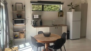 A modern kitchen with a round wooden table, black chairs, a white refrigerator, and a window with a view of greenery. - The Orchard & Oak Apartment - Pool, Peaceful, Perfect. (Te Puke)