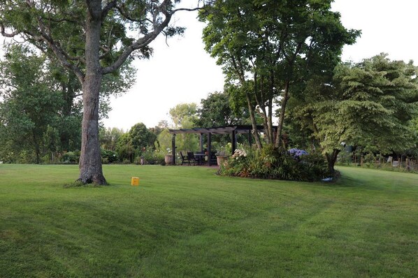 A well-maintained grassy area with a gazebo, trees, and a small table and chairs set up for outdoor dining.