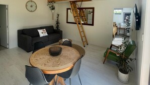 A modern living room with a round wooden table, a grey sofa, and a staircase with wooden railings. - The Orchard & Oak Apartment - Pool, Peaceful, Perfect. (Te Puke)