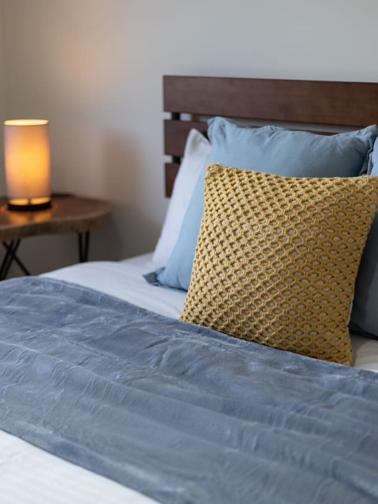 Un letto con un piumone grigio, una testiera in legno e due cuscini, uno con un motivo giallo e uno blu.