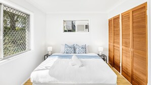 Ein Schlafzimmer mit einem großen Bett, weißen Wänden, einem Fenster mit Metallgitter, einer Deckenleuchte und Holzschränken.
