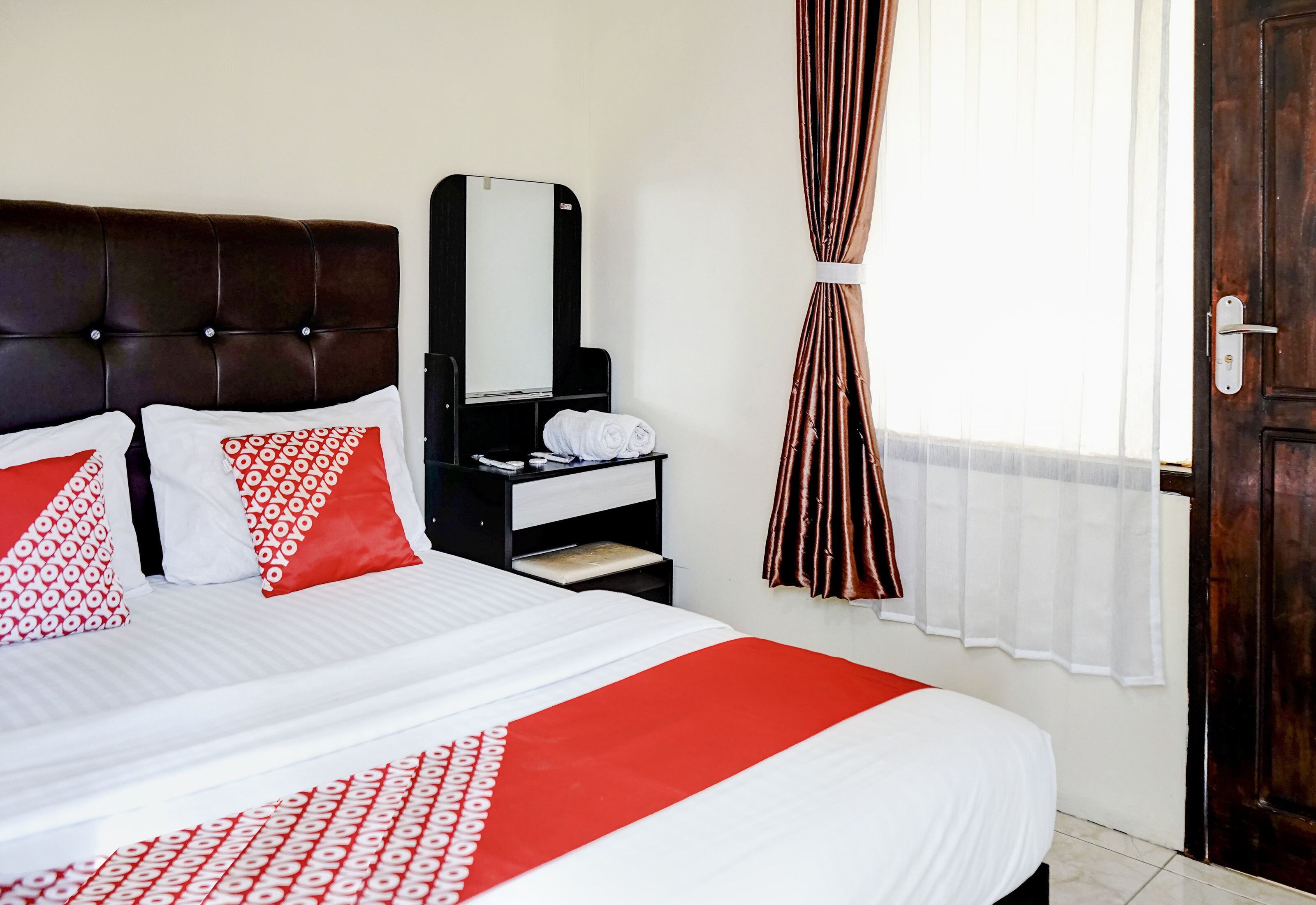 A hotel room with a bed, a nightstand, a mirror, a window with curtains, and a door.