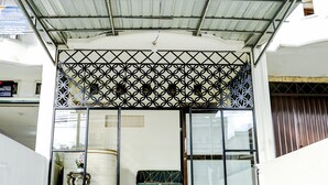 A building entrance with a geometric patterned metal gate, a large window with a patterned curtain, and a tiled floor. - Hotel O Mantari Guesthouse (Bukittinggi)