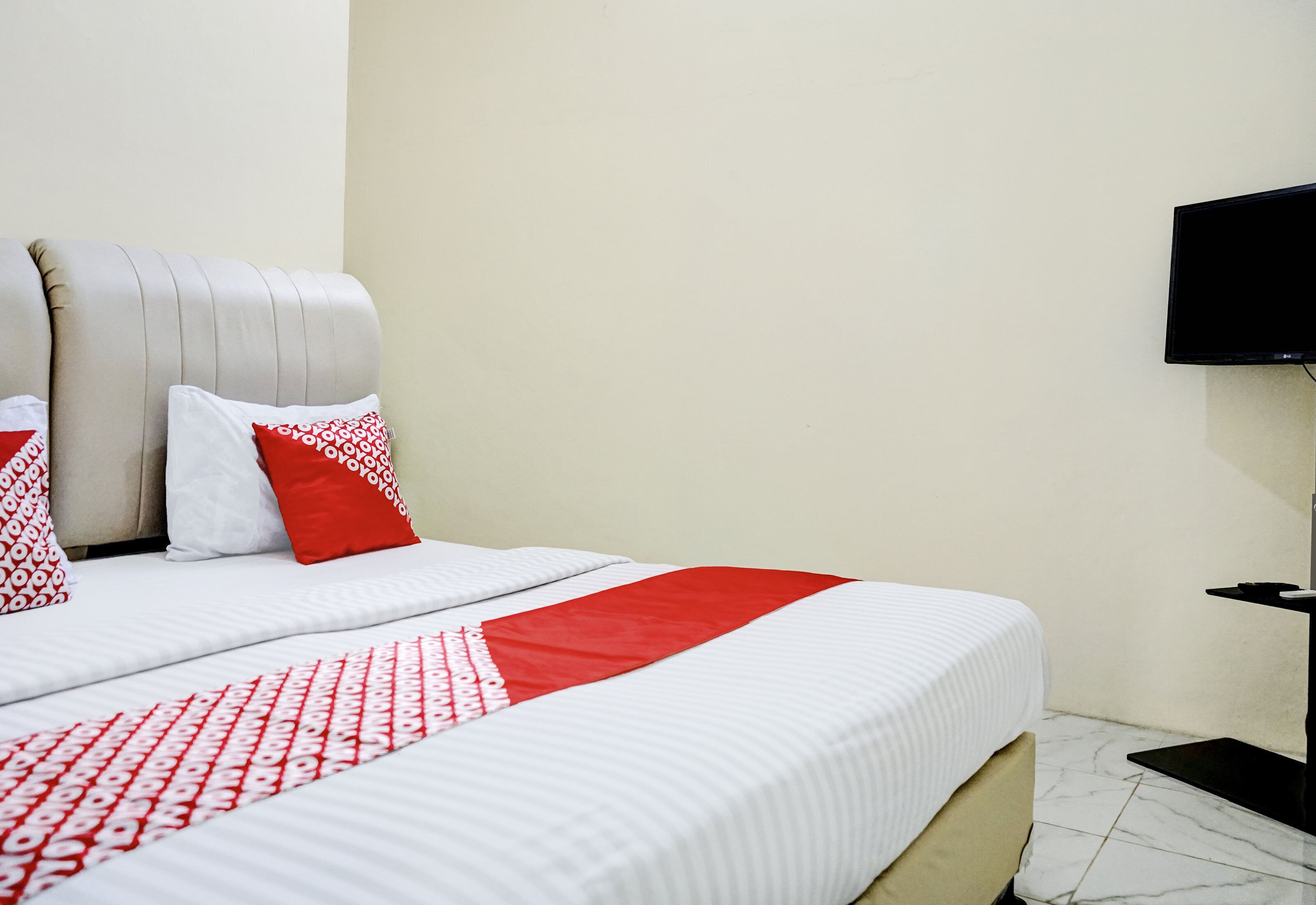 A hotel room with a bed, pillows, a television, and a small table.