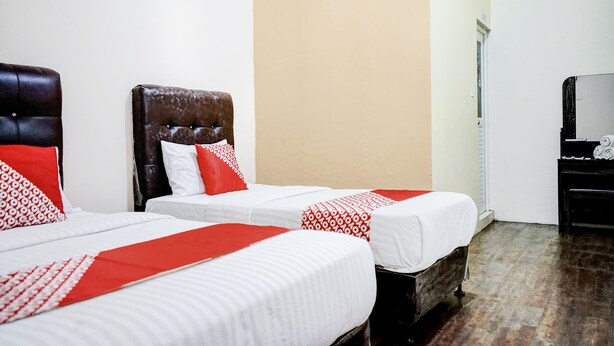 A hotel room with two beds, each with white bedding and red accents, a dark headboard, and a wooden floor. - Hotel O Mantari Guesthouse (Bukittinggi)