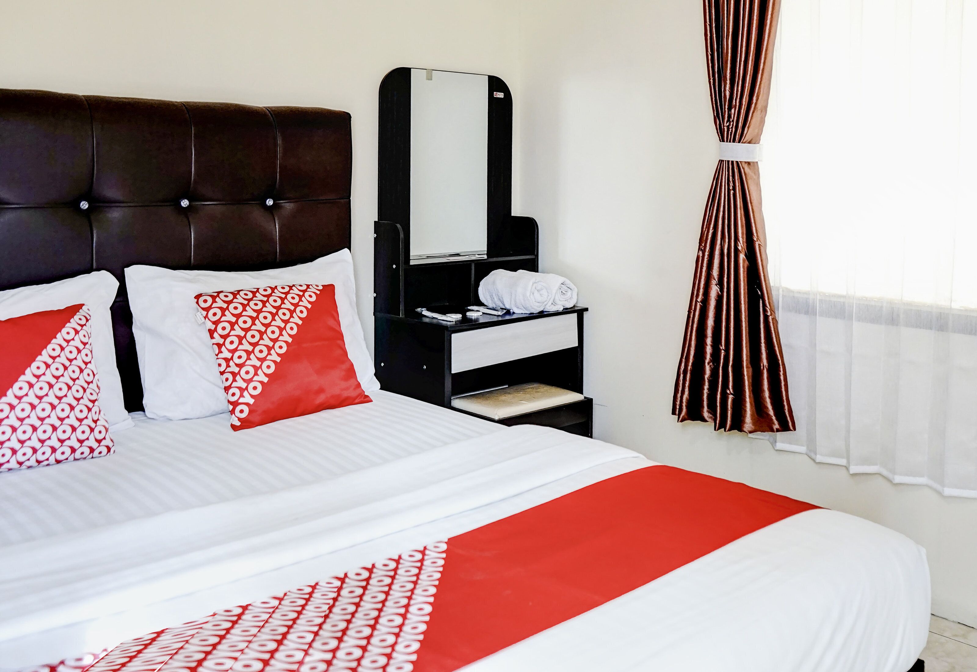 Een hotelkamer met een bed, nachtkastje, spiegel en raam met gordijnen.