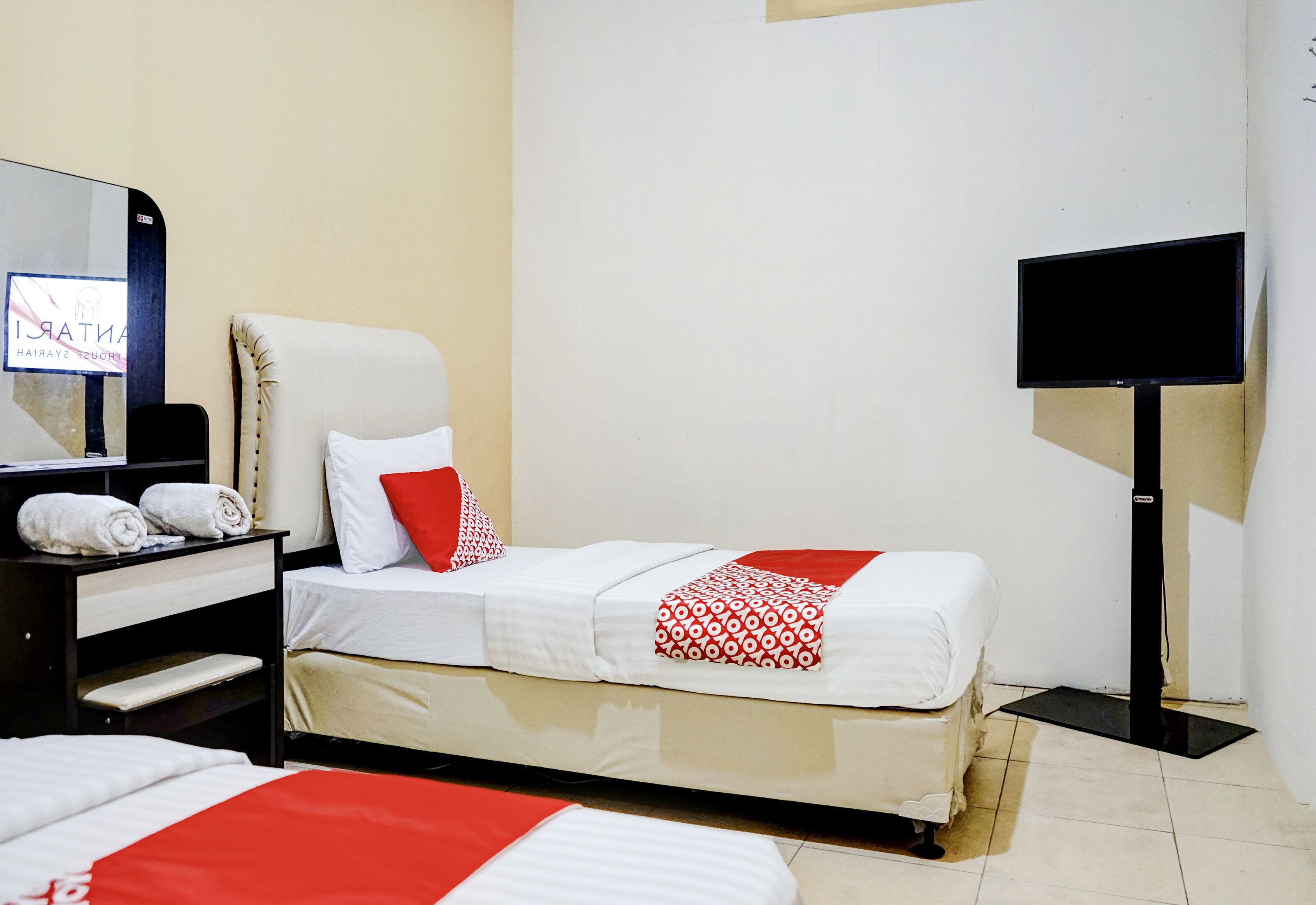 A hotel room with a bed, a TV, a mirror, and a desk with towels.