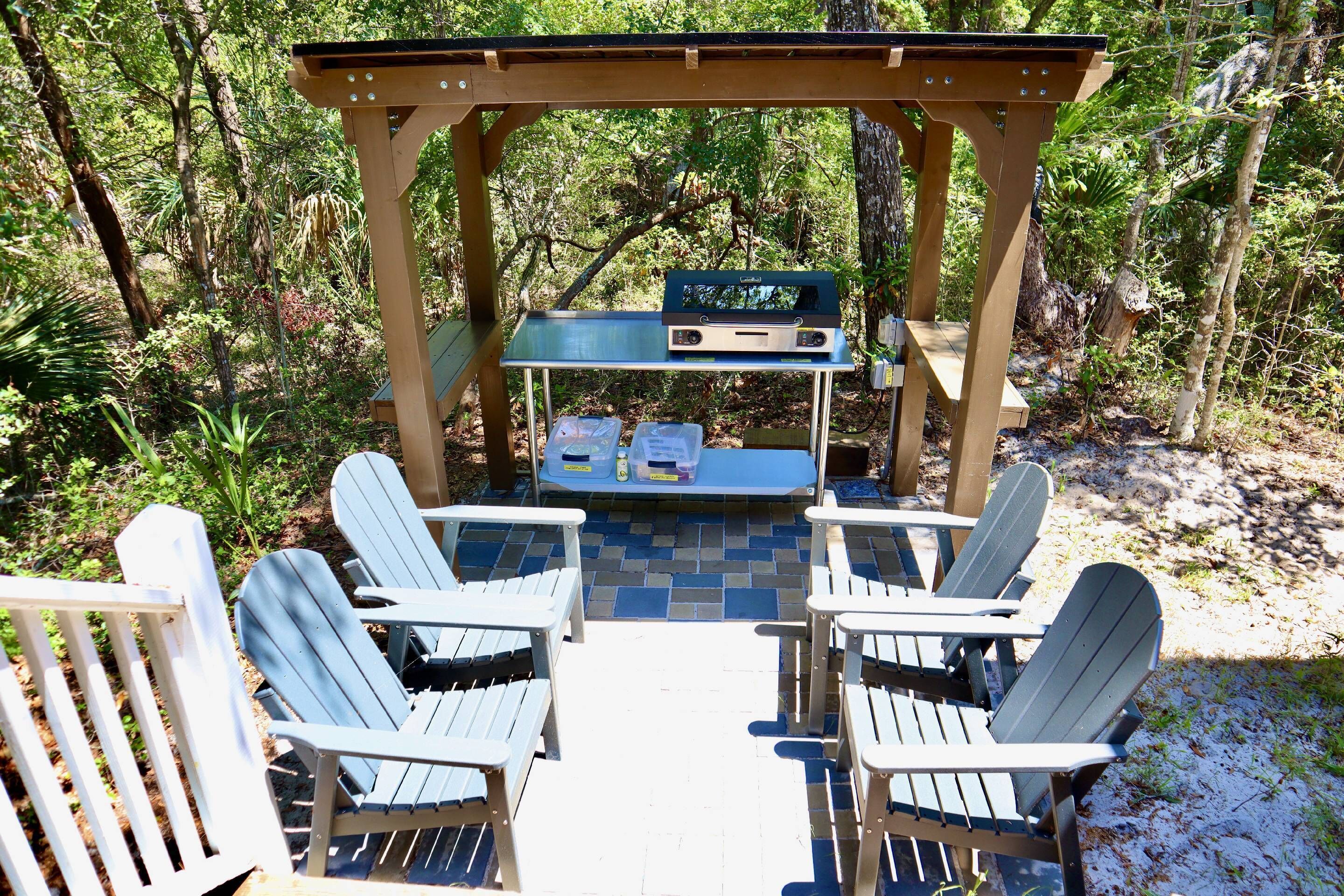 A wooden pergola with a built-in grill and seating area with Adirondack chairs.