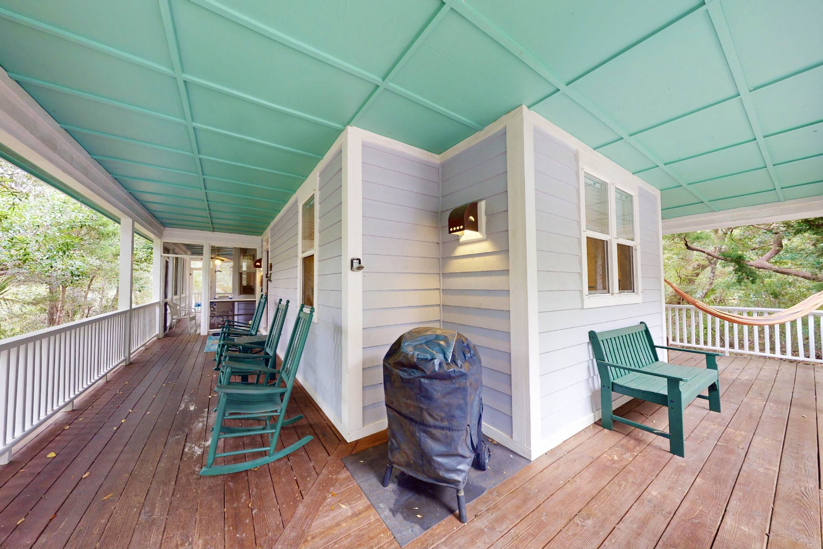 A covered porch with wooden flooring, green chairs, and a covered object.