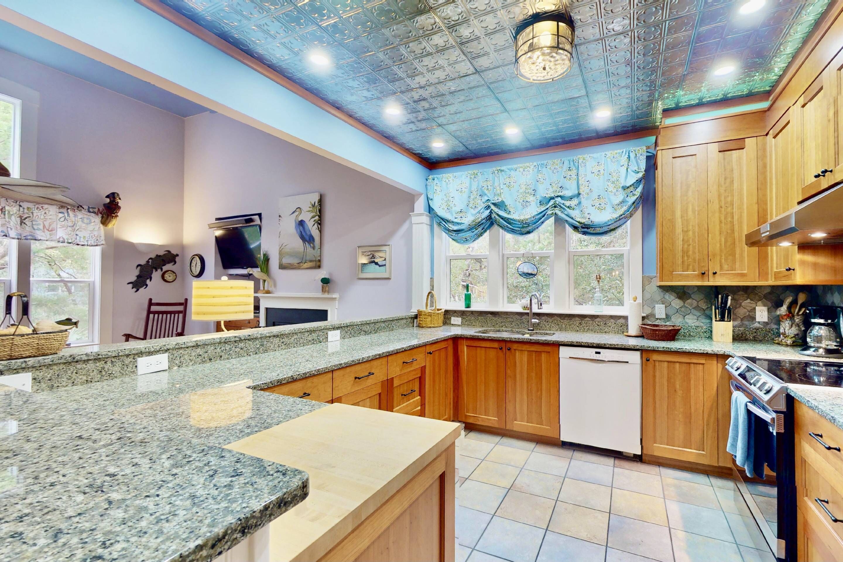A kitchen with granite countertops, wooden cabinets, a built-in oven, and a window with a blue curtain.