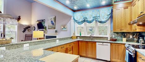 A kitchen with granite countertops, wooden cabinets, a built-in oven, and a window with a blue curtain.