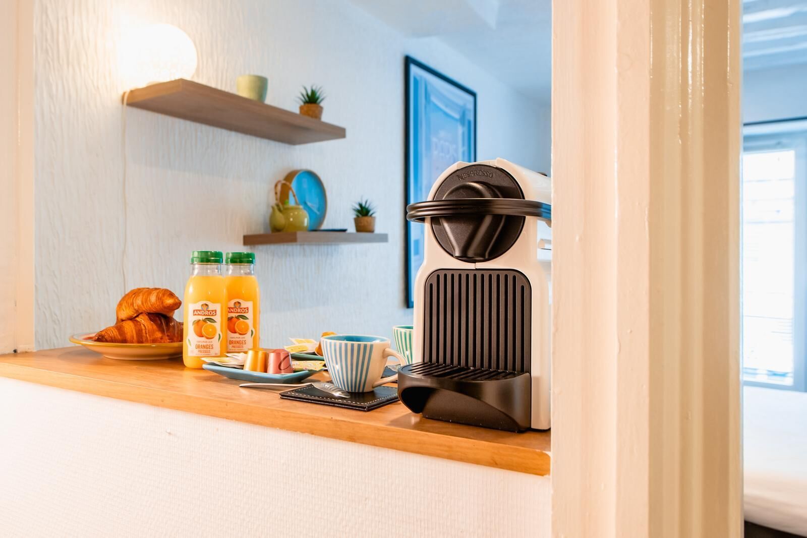 A kitchen counter with a coffee machine, orange juice, croissants, and a plate of food.
