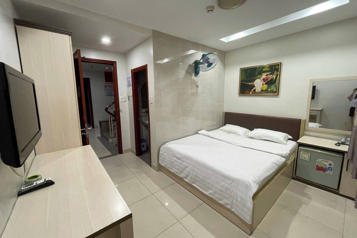 Une chambre d’hôtel équipée d’un lit, d’un bureau, d’une télévision, d’un ventilateur et d’un petit réfrigérateur.