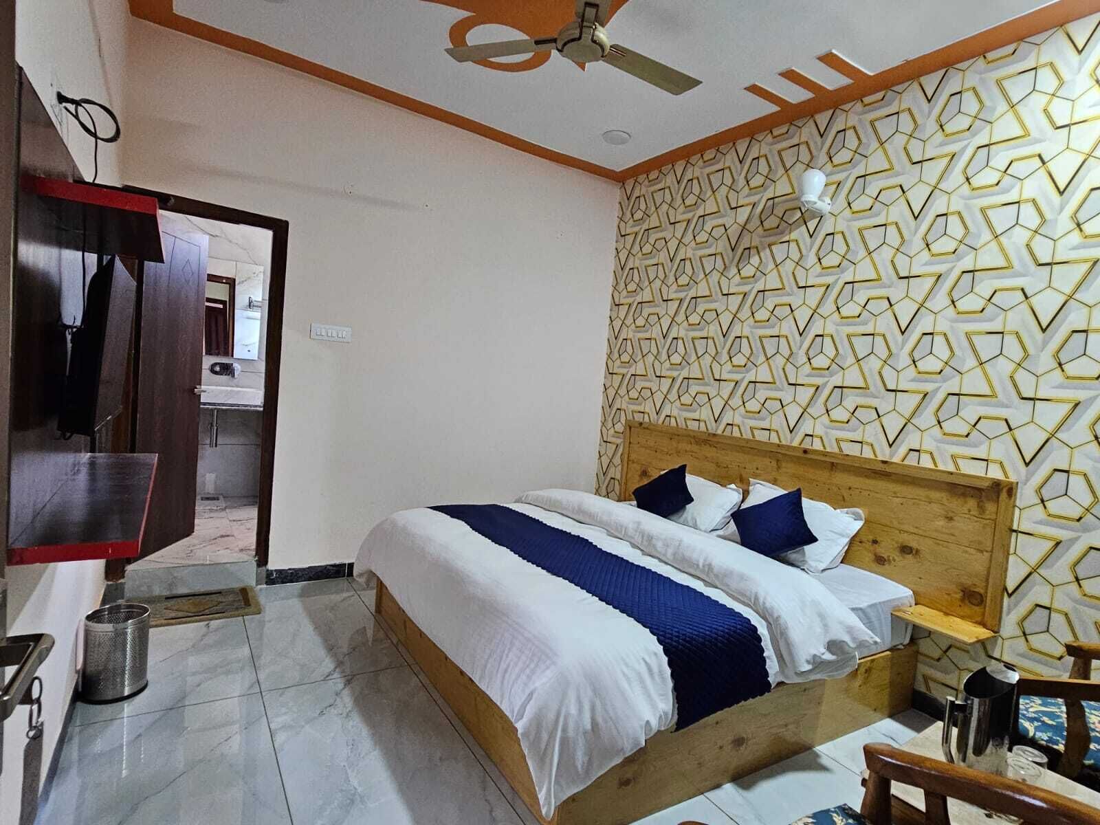 A bedroom with a wooden bed, a patterned wall, a ceiling fan, and a visible bathroom.
