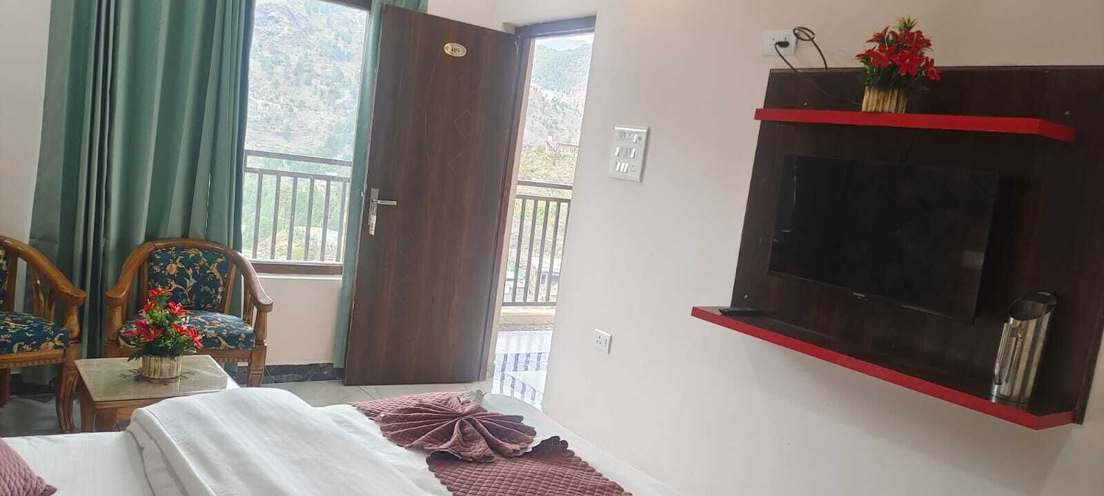 A room with a bed, a wooden chair, a TV mounted on the wall, and a balcony with a railing.