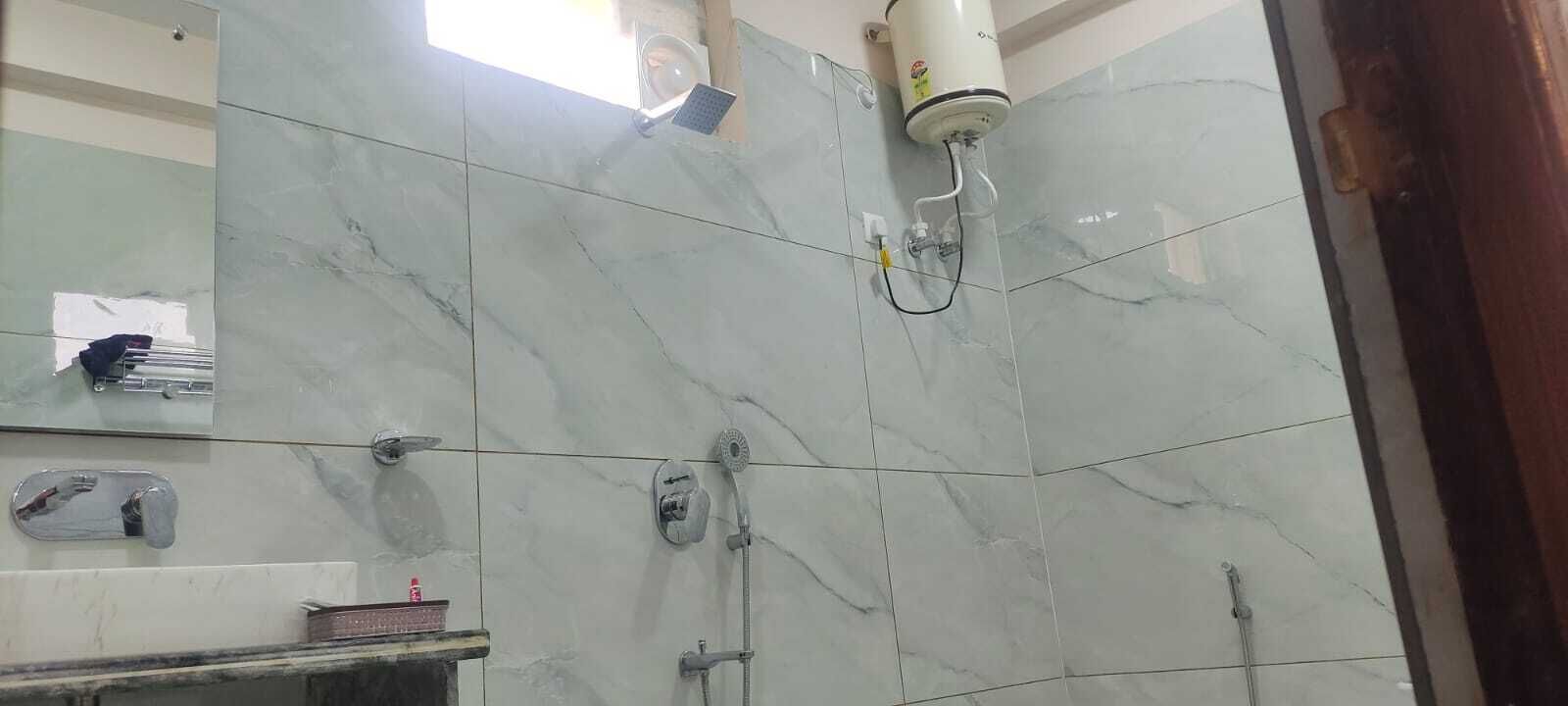 Un baño con azulejos de mármol, un secador de manos, un perchero para toallas y un cabezal de ducha.