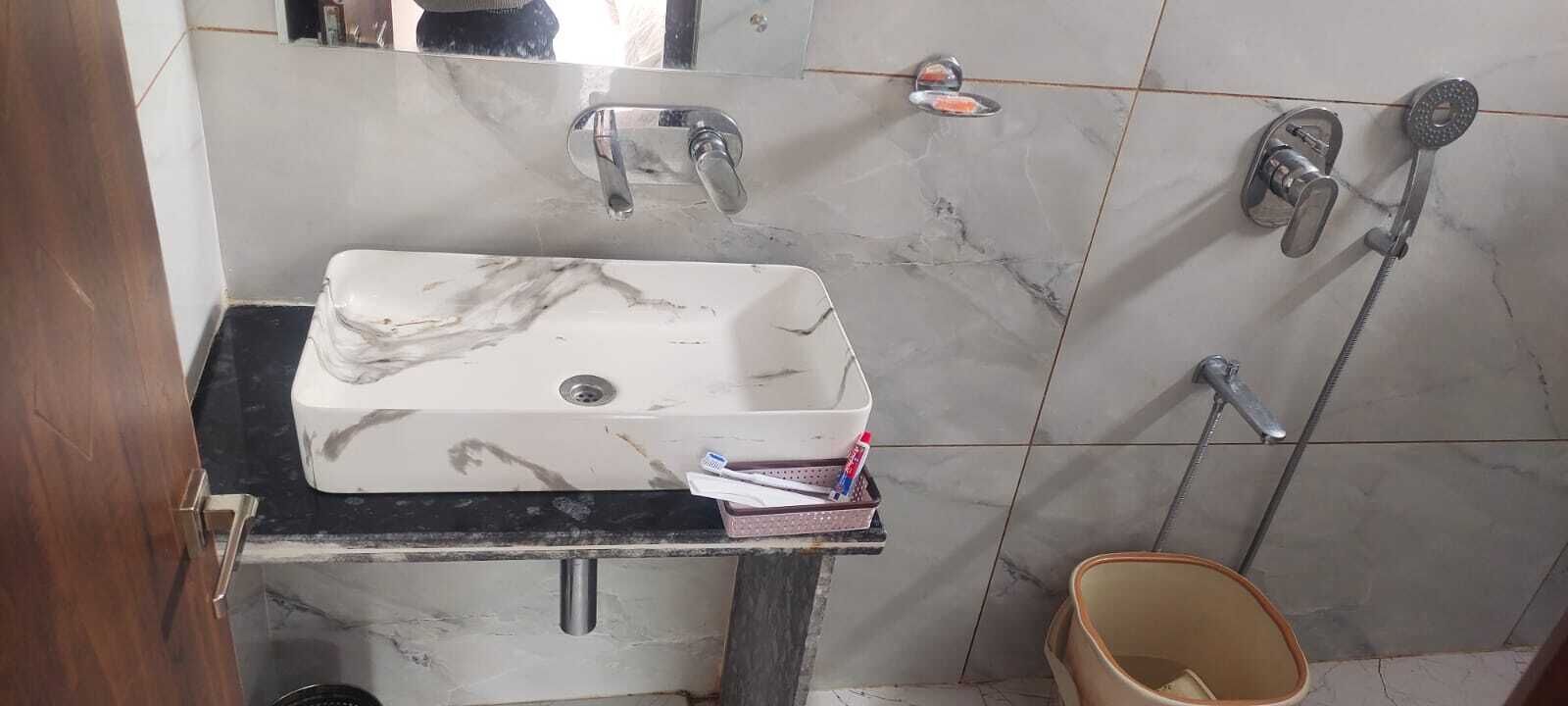 Un baño con lavamanos de mármol, un espejo, ducha e inodoro.