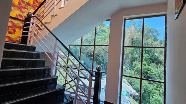 Eine Treppe mit Glasgeländer führt zu einem Raum mit großen Fenstern und Blick auf ein bewaldetes Gebiet.