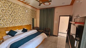 Ein Hotelzimmer mit einem Bett, einem Deckenventilator, einer gemusterten Wand, einem grünen Vorhang und einer Tür.