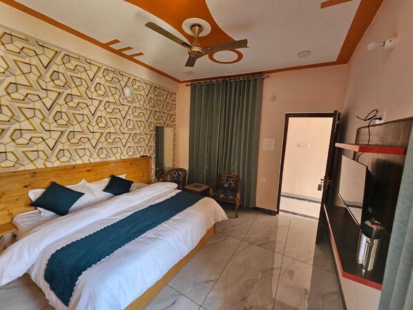 A hotel room with a bed, a ceiling fan, a patterned wall, a green curtain, and a door. - Hotel Necklace Moon Restaurants (Rajgarhi)