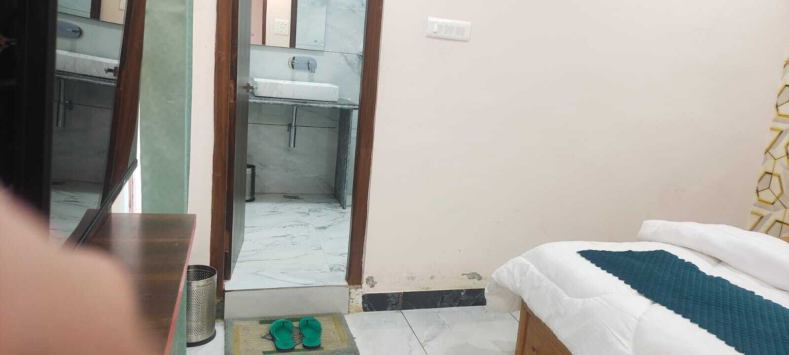A room with a bed, a small table, a mirror, and a bathroom visible through an open door.