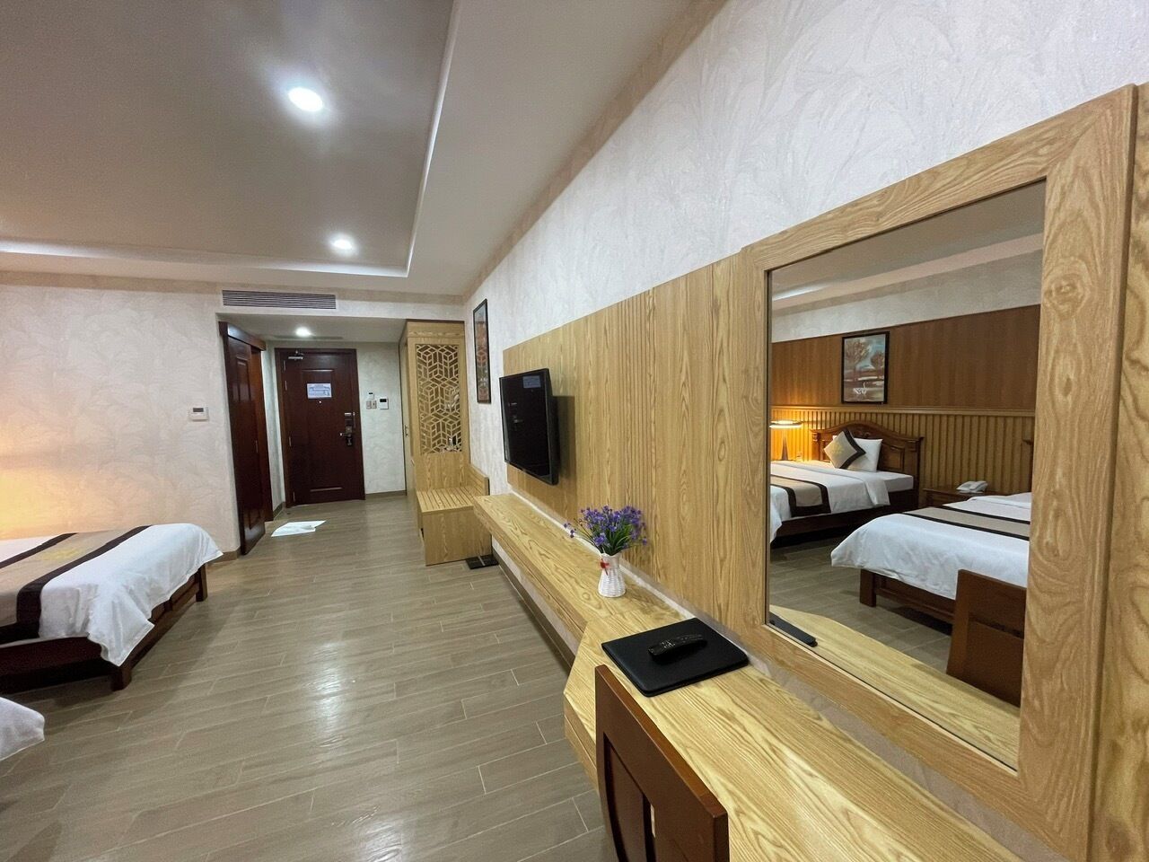 Ein Hotelzimmer mit Holzböden, einem großen Spiegel, einem Schreibtisch mit Blumen in einer Vase und drei Betten.