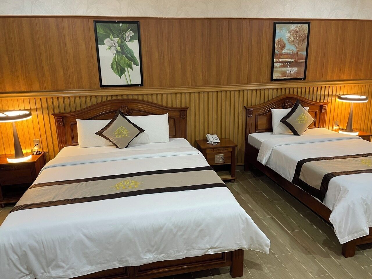 A hotel room with two beds, wooden headboards, white bedding, and two bedside lamps.