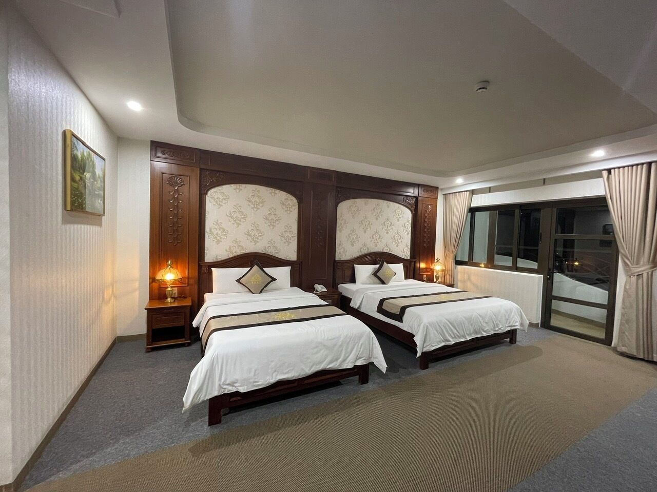 Habitación de hotel con dos camas, un ventanal con cortinas y vistas al exterior.