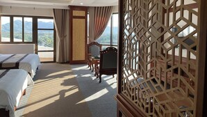A hotel room with two beds, a desk, and a chair. There is a large window with a view of mountains. - Rex Hotel Binh Dinh - by BAY LUXURY (Binh Dinh)
