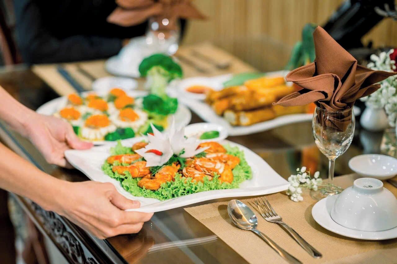 A dining table with plates of food, a folded napkin, a glass of water, and a spoon.