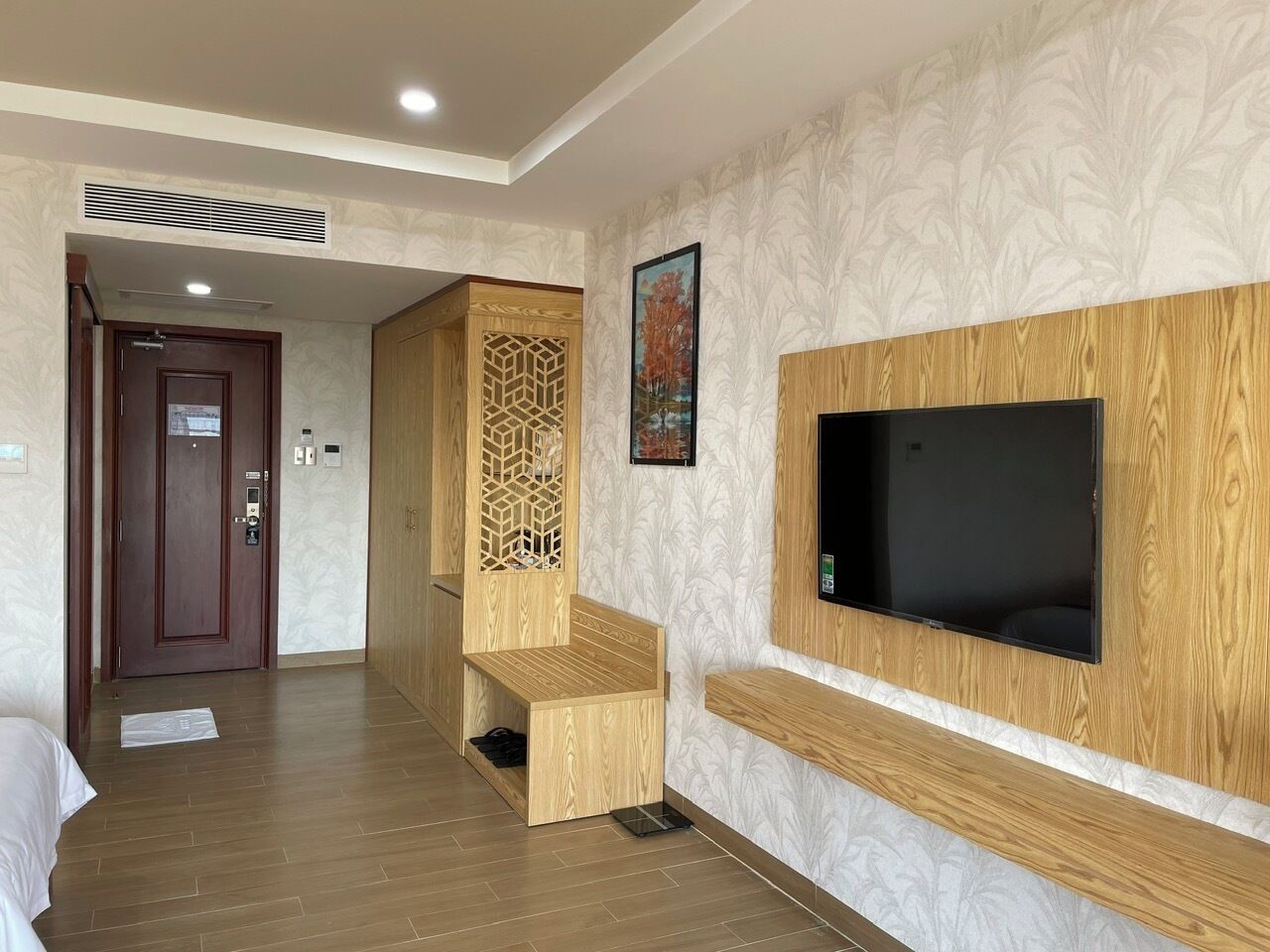 Una camera d'albergo con pavimento in legno, una TV fissata al muro, una panca in legno e una porta che conduce a un'altra stanza.