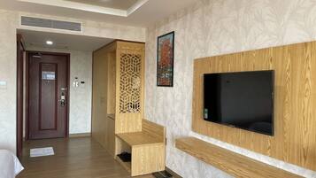 Una camera d'albergo con pavimento in legno, una TV fissata al muro, una panca in legno e una porta che conduce a un'altra stanza.