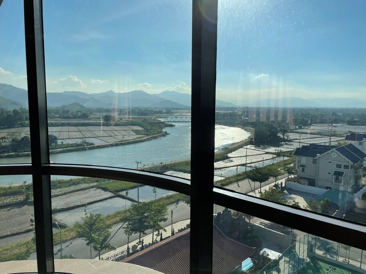 A view from a window overlooking a river, fields, and a building. - Rex Hotel Binh Dinh - by BAY LUXURY (Binh Dinh)
