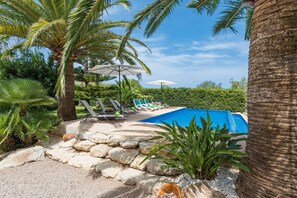 A pool area with lounge chairs and umbrellas, surrounded by palm trees and greenery. - Casa Angela - Villa With Private Pool In Capdepera (Capdepera, Illes Balears)