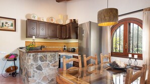 Une cuisine dotée d’un îlot en pierre, de chaises en bois, d’un réfrigérateur en acier inoxydable et d’un luminaire suspendu.
