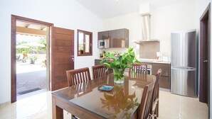 A dining area with a glass table, wooden chairs, a vase with flowers, a microwave, a refrigerator, and a kitchen counter. - Can Melis - Villa With Private Pool In Campanet (Campanet, Illes Balears)