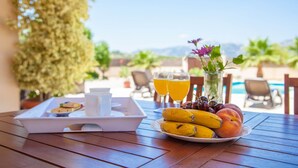 A breakfast tray with fruits and juice glasses on a wooden table with a pool view. - Can Melis - Villa With Private Pool In Campanet (Campanet, Illes Balears)
