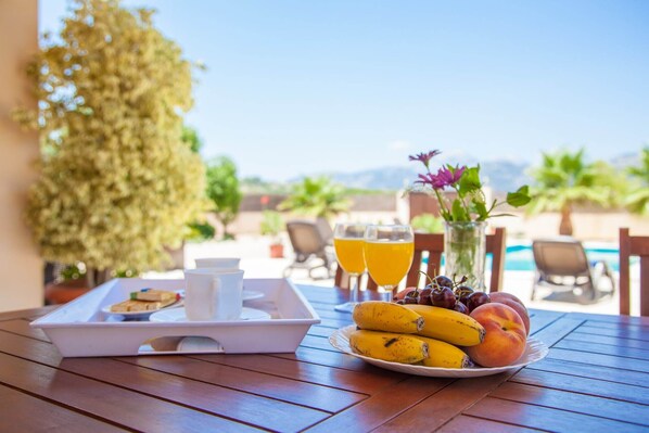 A breakfast tray with fruits and juice glasses on a wooden table with a pool view.