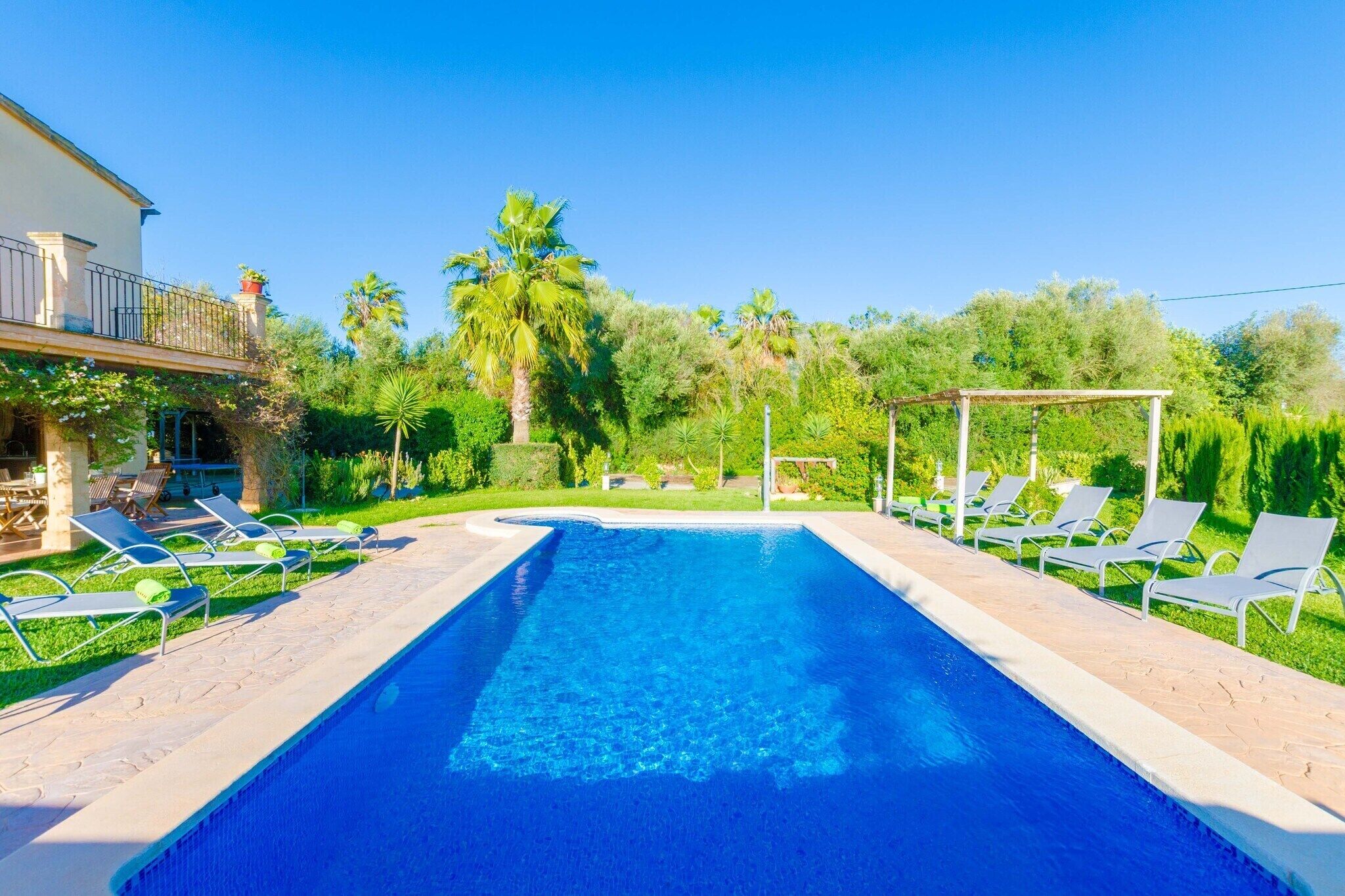 Una piscina rectangular con agua azul cristalina, rodeada por una terraza empedrada. Hay sillas de descanso alineadas a lo largo del borde de la piscina.