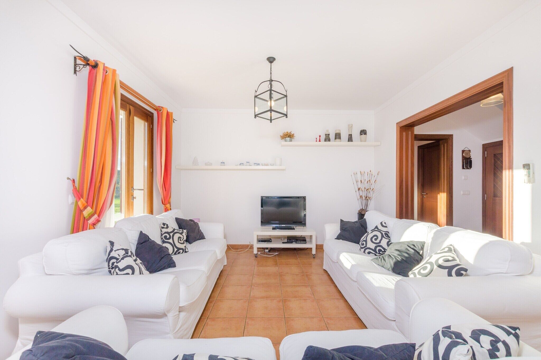 A living room with two white sofas, a TV on a stand, and a ceiling light.