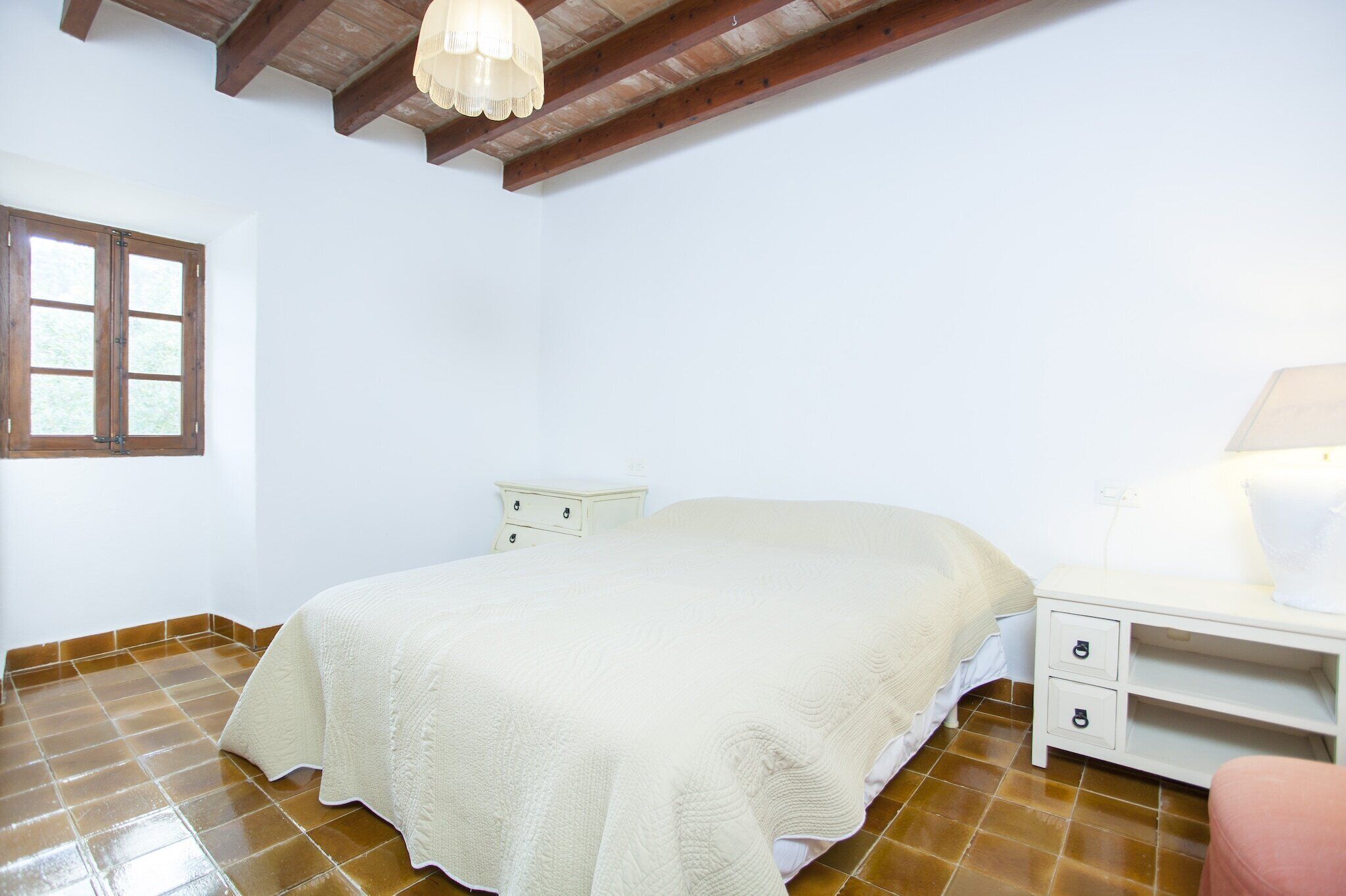 A bedroom with a bed, a nightstand, a lamp, and a window.
