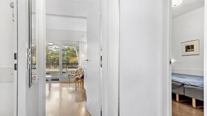 A hallway leading to a room with a bed, a framed picture on the wall, and a view of an outdoor area with a table and chairs.
